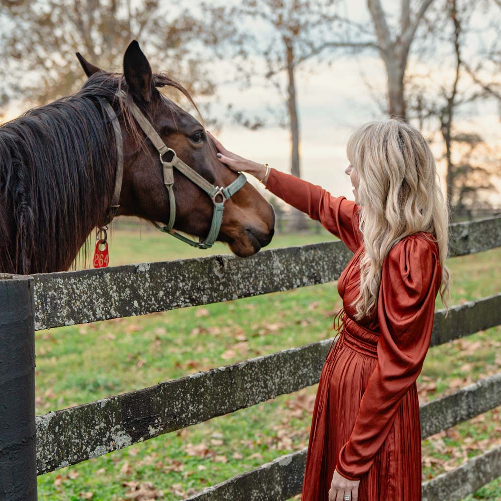 Owner Jennifer Jewett smiling and engaging with a horse in a Lexington paddock