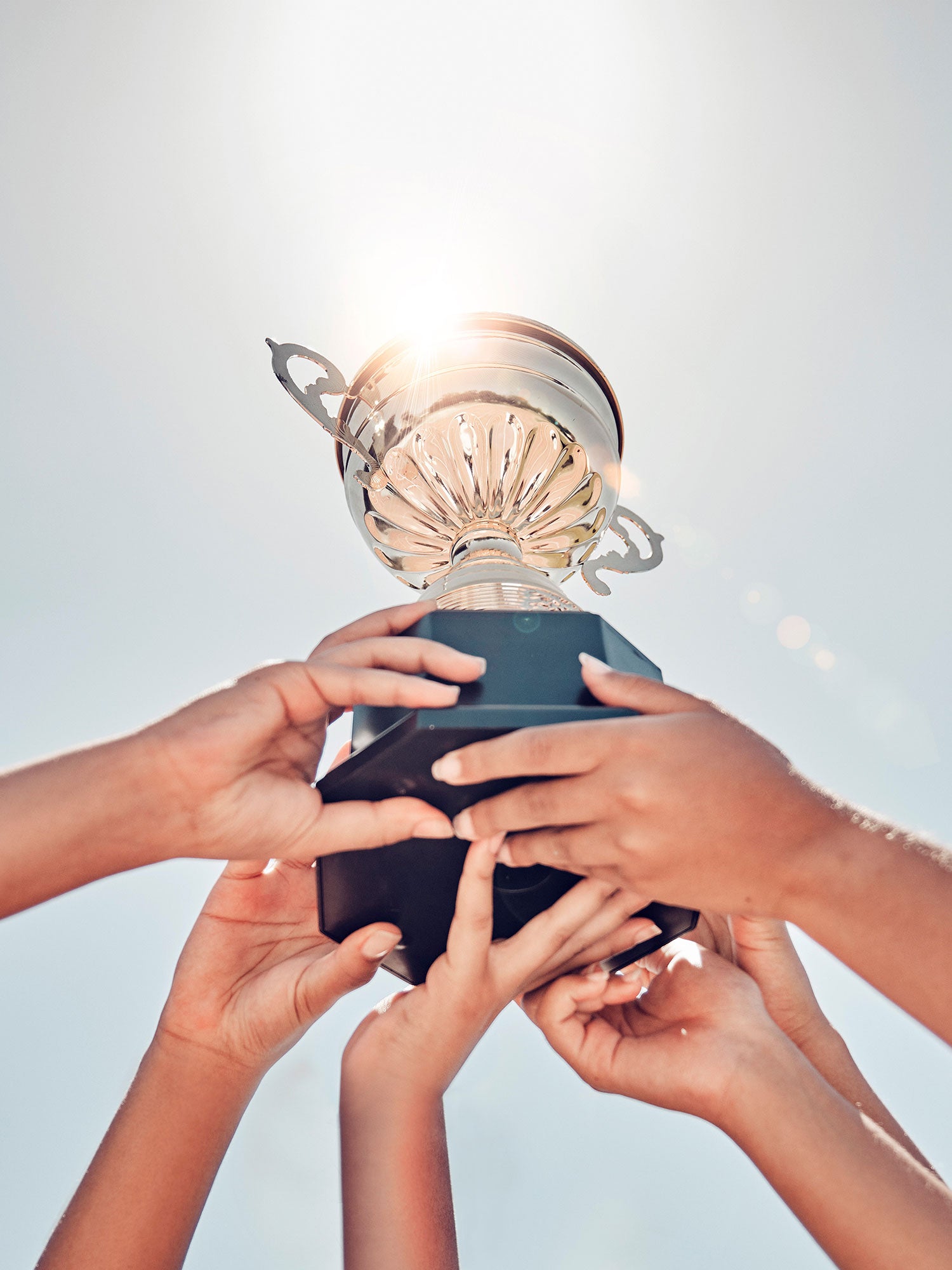 A Trophy Being Held High In The Sky By 3 Sets Of Hands